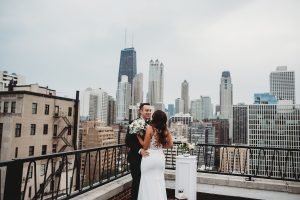 bride and groom hugging on roof top with Chicago skyline behind them