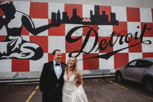 bride and groom walking and laughing by detroit mural in detroit