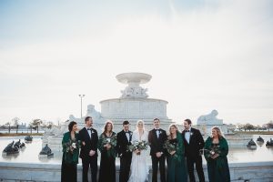 wedding party sitting on the edge of the belle isle fountain smiling