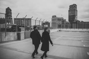 couple walking in the wind on top of the z lot Detroit mi engagement photos