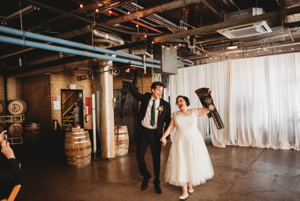 bride and groom walking into wedding reception laughing and holding WWE belts whiskey factory detroit mi