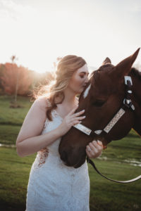 bride in wedding dress with her horse on a farm at sunset