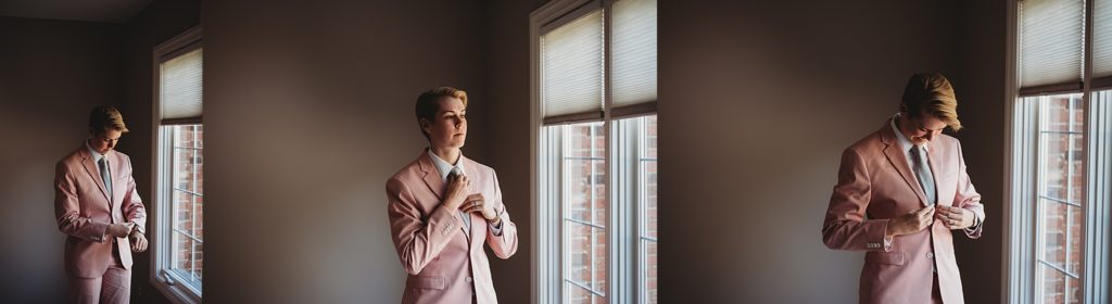 bride in a pink suit buttoning it up and smiling by a window