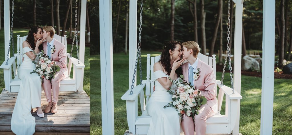 bride in a pink suit and bride in a white dress cuddling and kissing on a white garden swing holding pink and white wedding flowers 