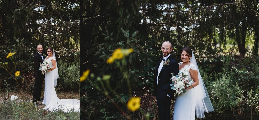 groom in a Yamaka and bride in a white lace dress smiling and laughing with each other in the woods. Bride holding a pink rose bouquet