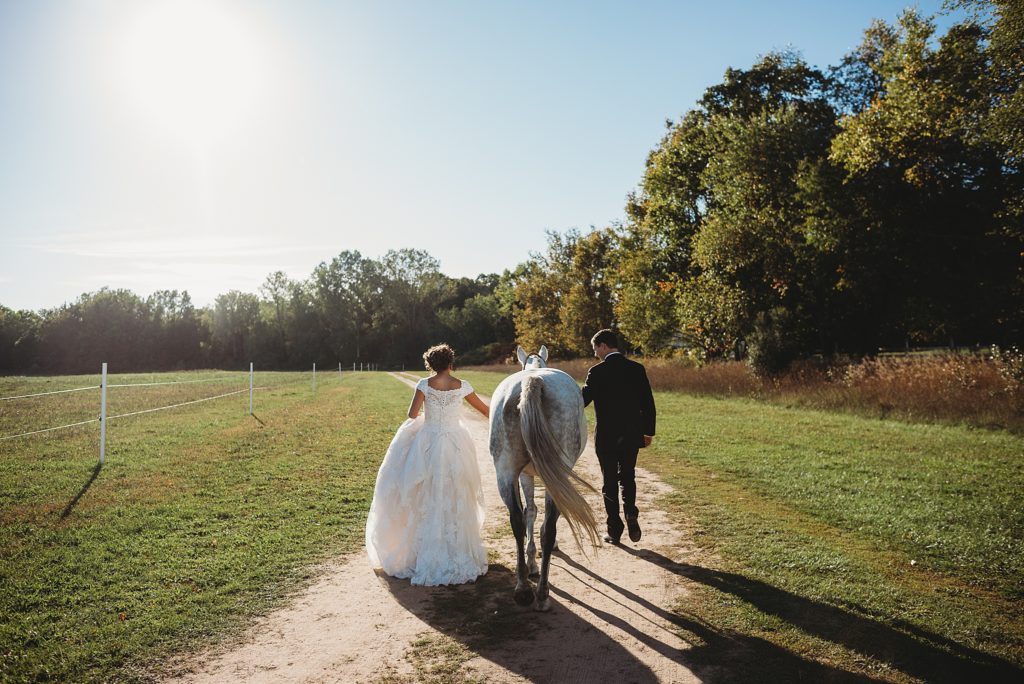 bride and groom walking into the sunset with their white horse