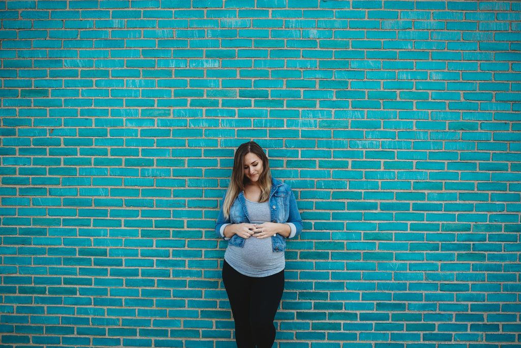 pregnant mom holding her belly against a teal brick wall