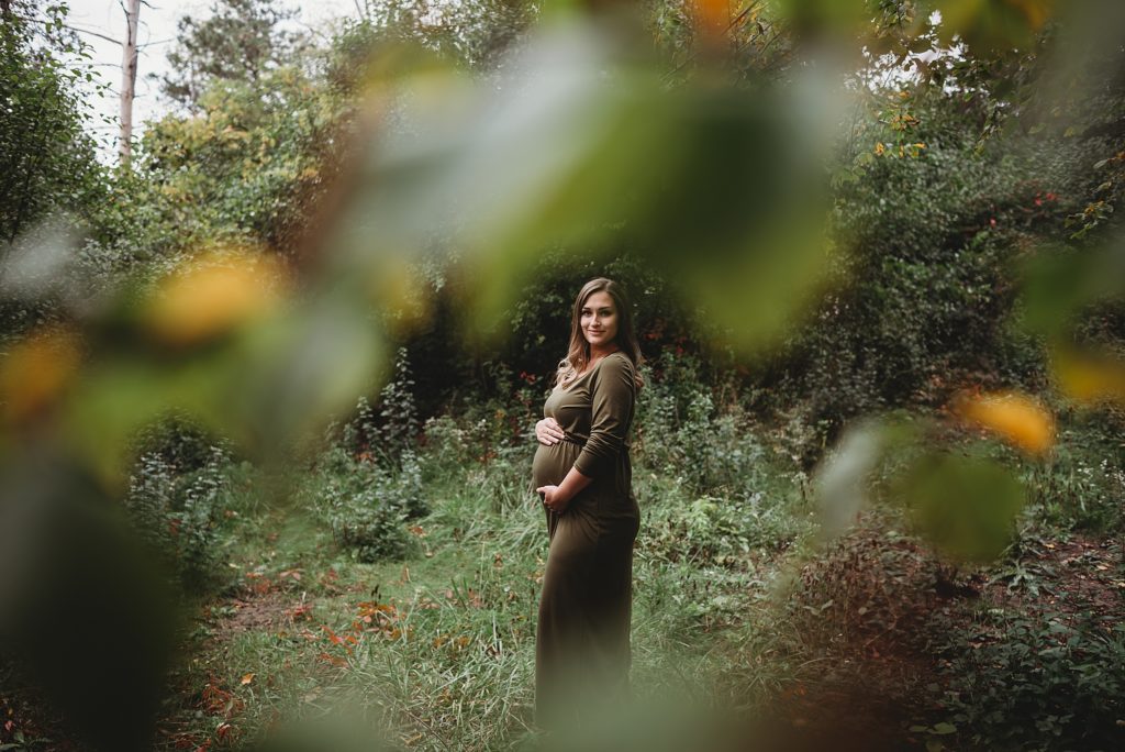 pregnant mom in a green dress holding her belly and smiling in the woods