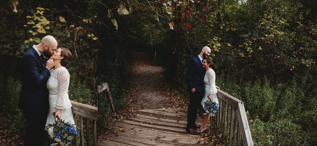 bride and groom kissing on a bridge in the woods