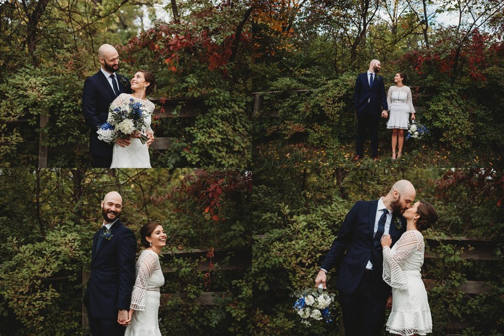 bride in a short white lace dress and groom in a navy suit laughing and kissing by the fall leaves