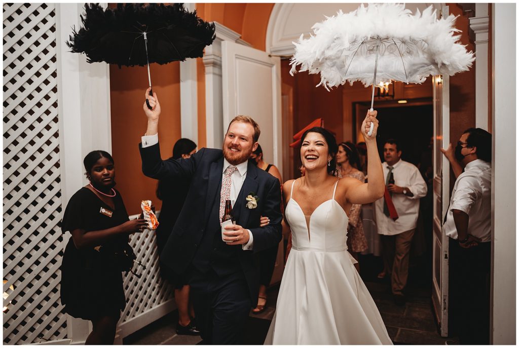bride and groom laughing and walking out of their reception with black and white umbrellas 