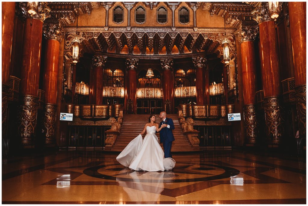 newly wed couple dancing in the grand foyer of the fox theatre. groom is wearing a navy blue suit and the bride is wearing a large white satin ball gown.  taken by one of the top wedding photographers in Detroit 