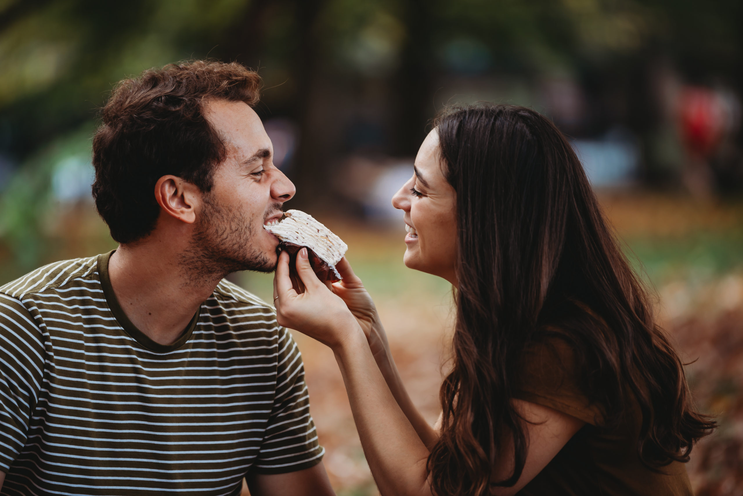 couple feeding one another cake in a park in the fall